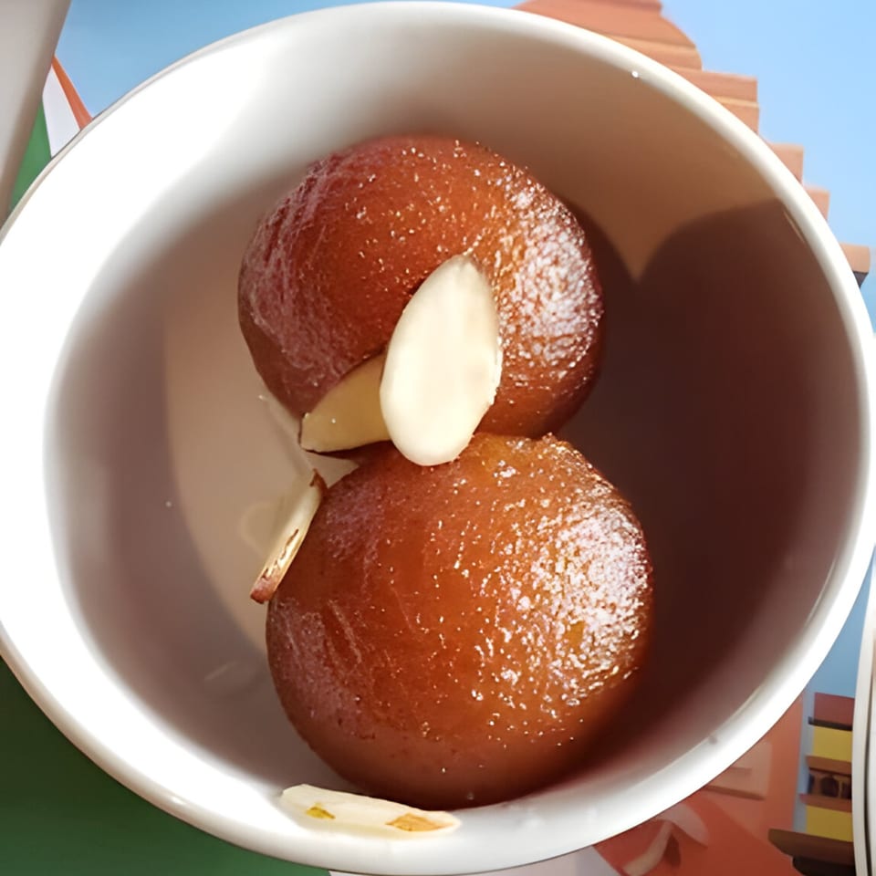 Two gulab jamun, Indian fried dough balls in syrup, garnished with almond slivers in a white bowl.