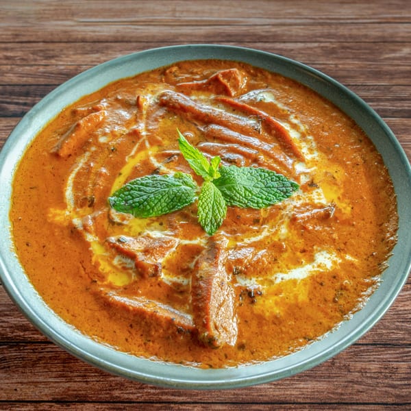 Rich orange Indian curry with chicken pieces, drizzled with cream and garnished with fresh mint.