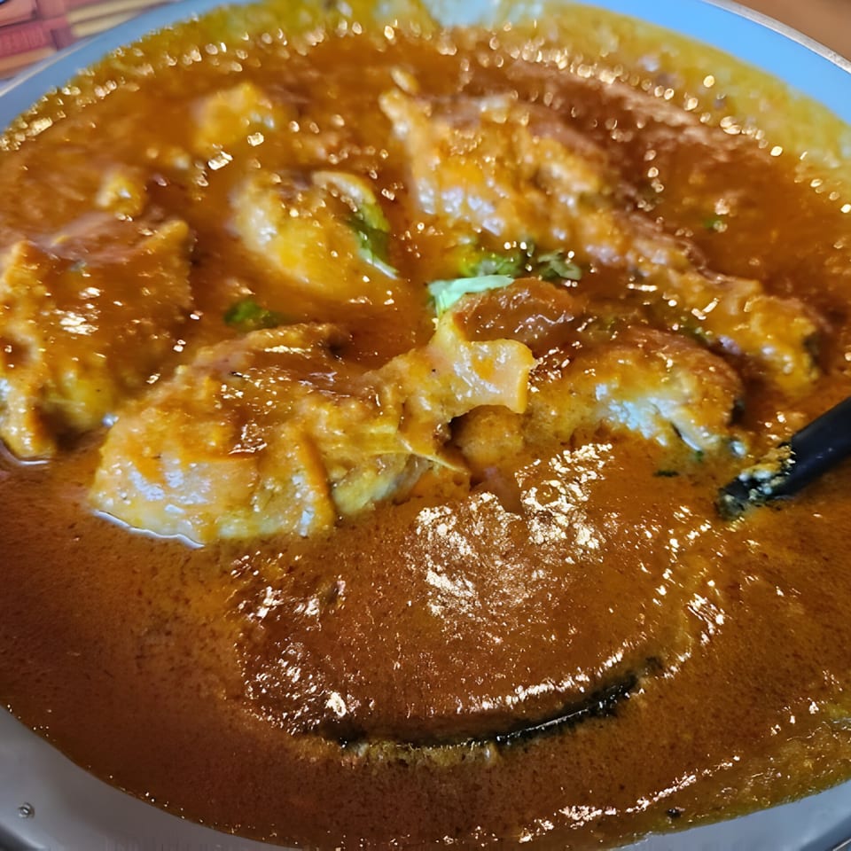Close-up of VEDA's Indian chicken curry, rich orange with tender chicken pieces and a spoon.