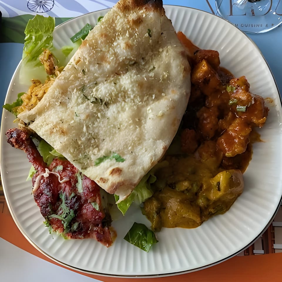 A white plate with Indian food, including naan, chicken tikka, curry, and rice.