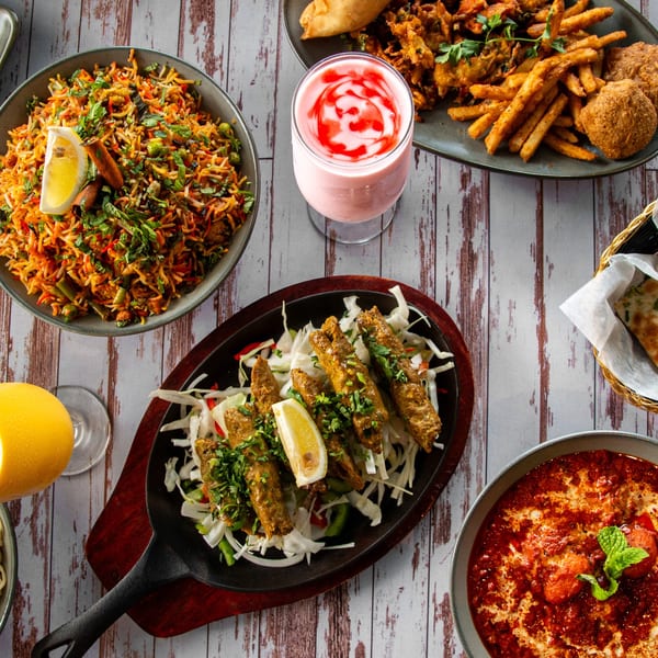Overhead view of various Indian dishes including biryani, kebabs, curry, fries, and a pink drink.