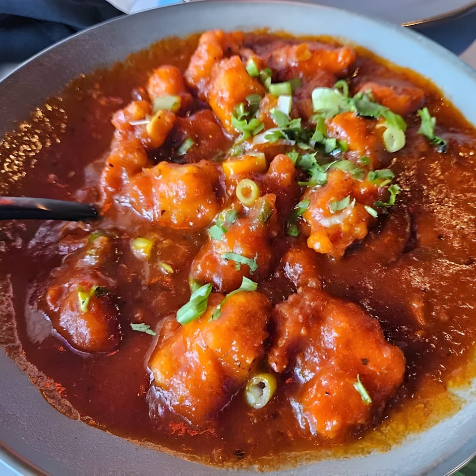 A close-up of VEDA INDIAN CUISINE & BAR's chili chicken, garnished with green onions and cilantro.